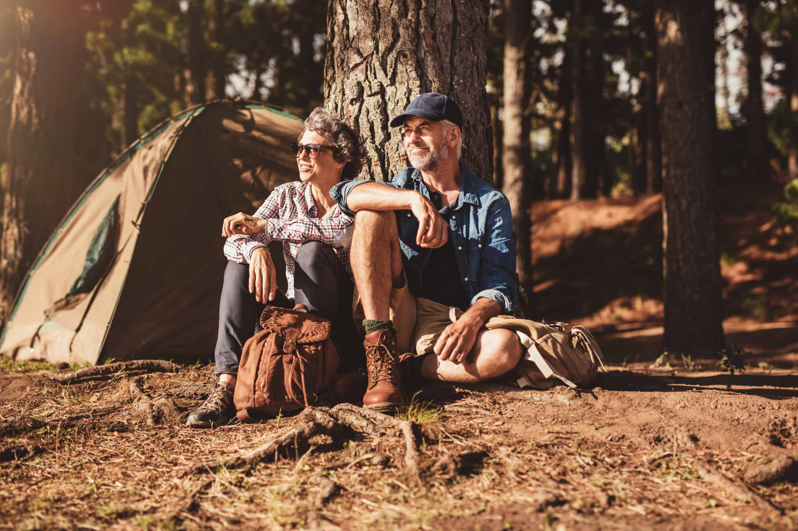 Portrait of senior couple sitting together under a tree in forest and looking at a view. Mature man and woman relaxing at their campsite.